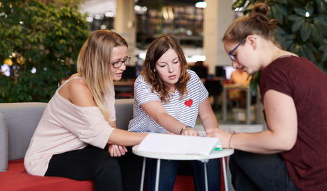 Drei junge Studentinnen lernen gemeinsam in der Bibliothek.