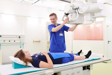 Herr Funke positioniert ein Röntgengerät über einer Patientin.